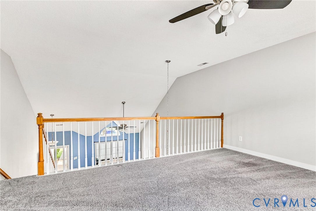 Carpeted loft space with a vaulted ceiling, ceiling fan, and wood and white spindle railing