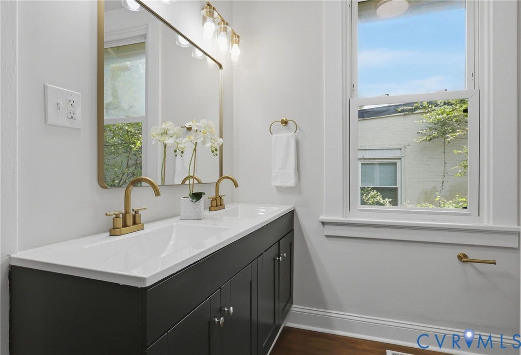 1815 Carlisle Avenue, Richmond, VA 23231 Dual vanity with brass-finish faucets, white countertop, dark cabinetry, and gold-framed mirror with integrated lighting