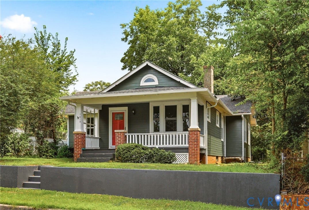 1815 Carlisle Avenue, Richmond, VA 23231 Front porch with brick piers and white columns, dark siding exterior, red entry door, gable roofline, and a gray retaining wall with integrated steps