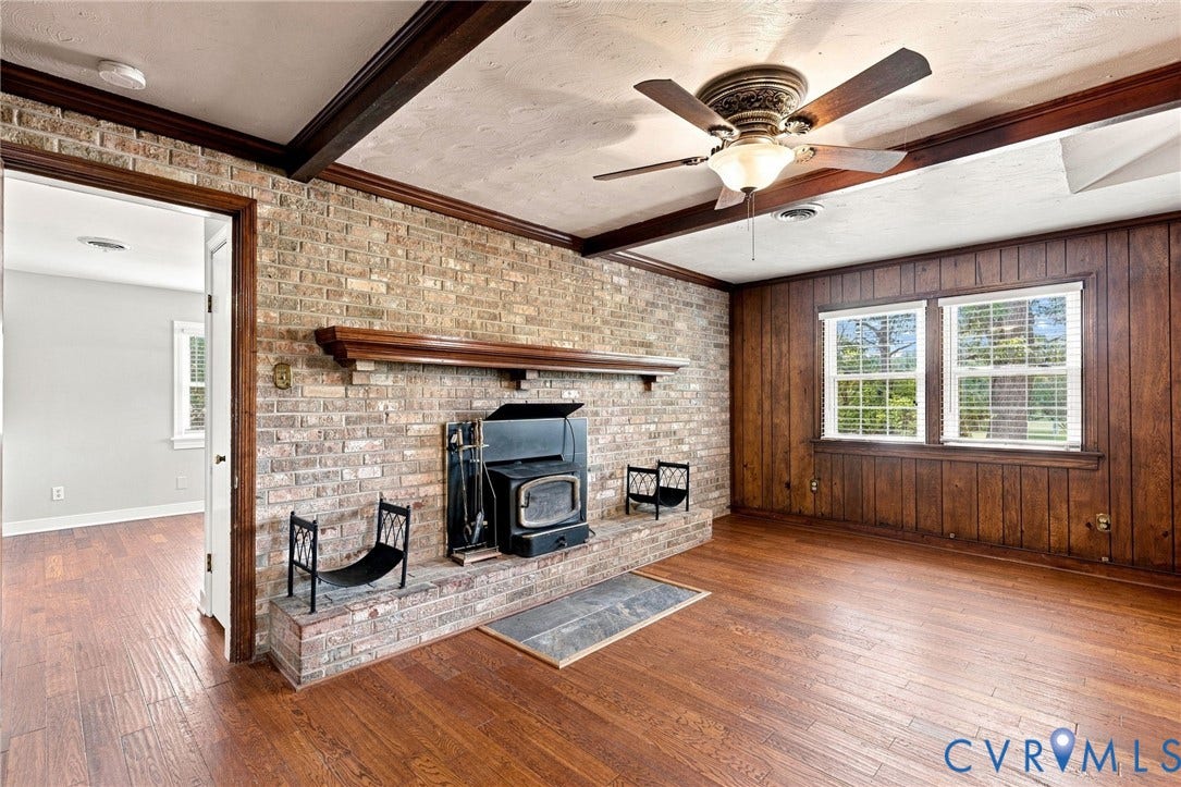 2707 Academy Road, Powhatan, VA 23139 Brick fireplace with wood stove insert, hardwood flooring, wood-paneled wall, wood beam ceiling, and a ceiling fan with integrated lighting
