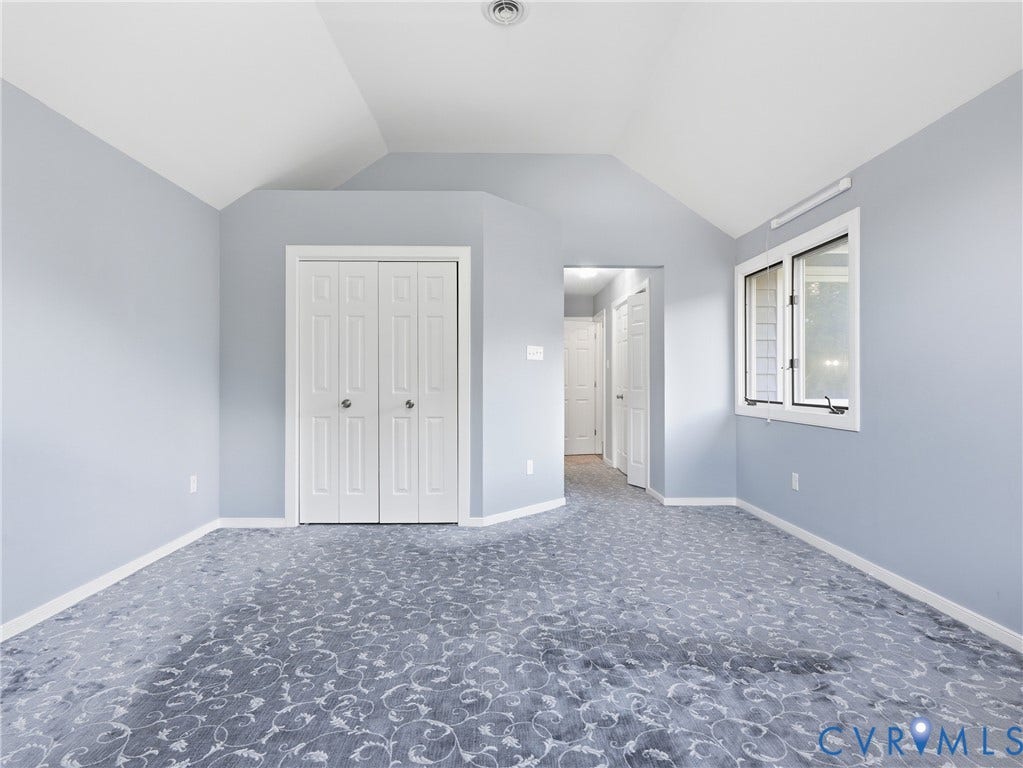 Vaulted ceiling with a ceiling-mounted light fixture, patterned carpet flooring, bi-fold closet doors, and a double window with white trim