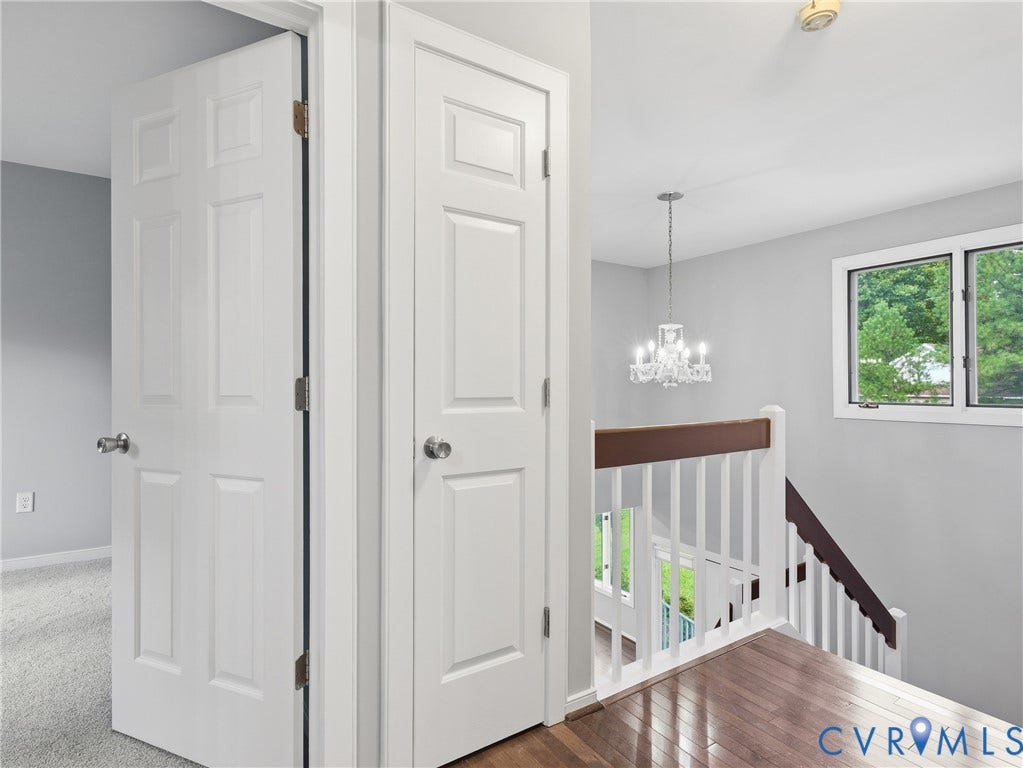 Upper landing with hardwood flooring, a modern chandelier, and a large window
