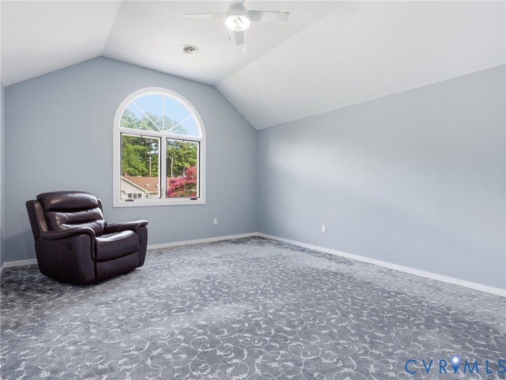 Arched window, vaulted ceiling, patterned carpeting, ceiling fan, and light blue wall finish
