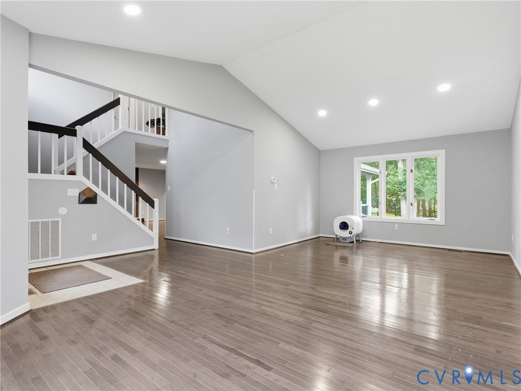Vaulted ceilings with recessed lighting, wood-finish flooring, staircase with dark wood handrails, and large windows