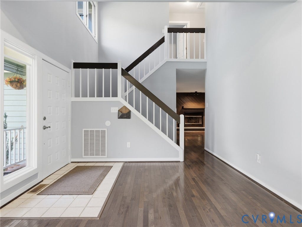 Foyer with wood-finish flooring, a white paneled entry door, and a staircase with white balusters and dark wood railings