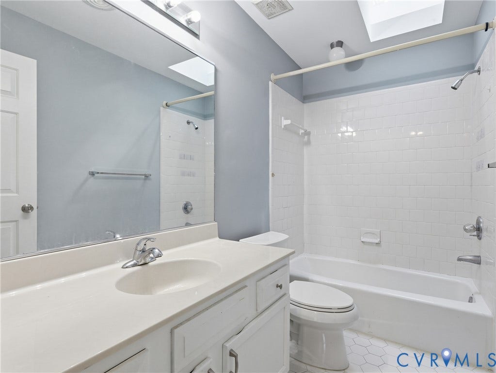 Bathroom featuring a white vanity with integrated sink, chrome faucet, wall-mounted mirror, white subway tile tub surround, and hexagon tile flooring