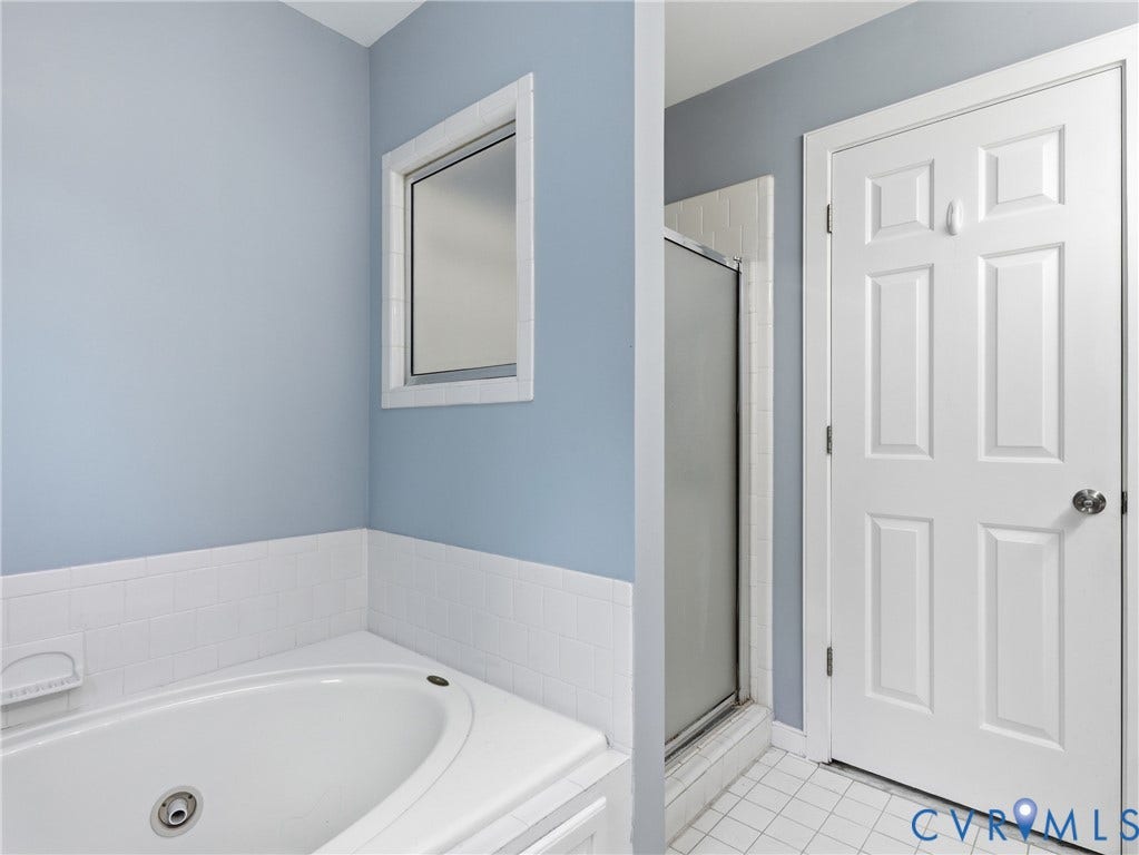 Corner soaking tub, white subway tile wainscoting, framed window, paneled door, and glass-enclosed shower