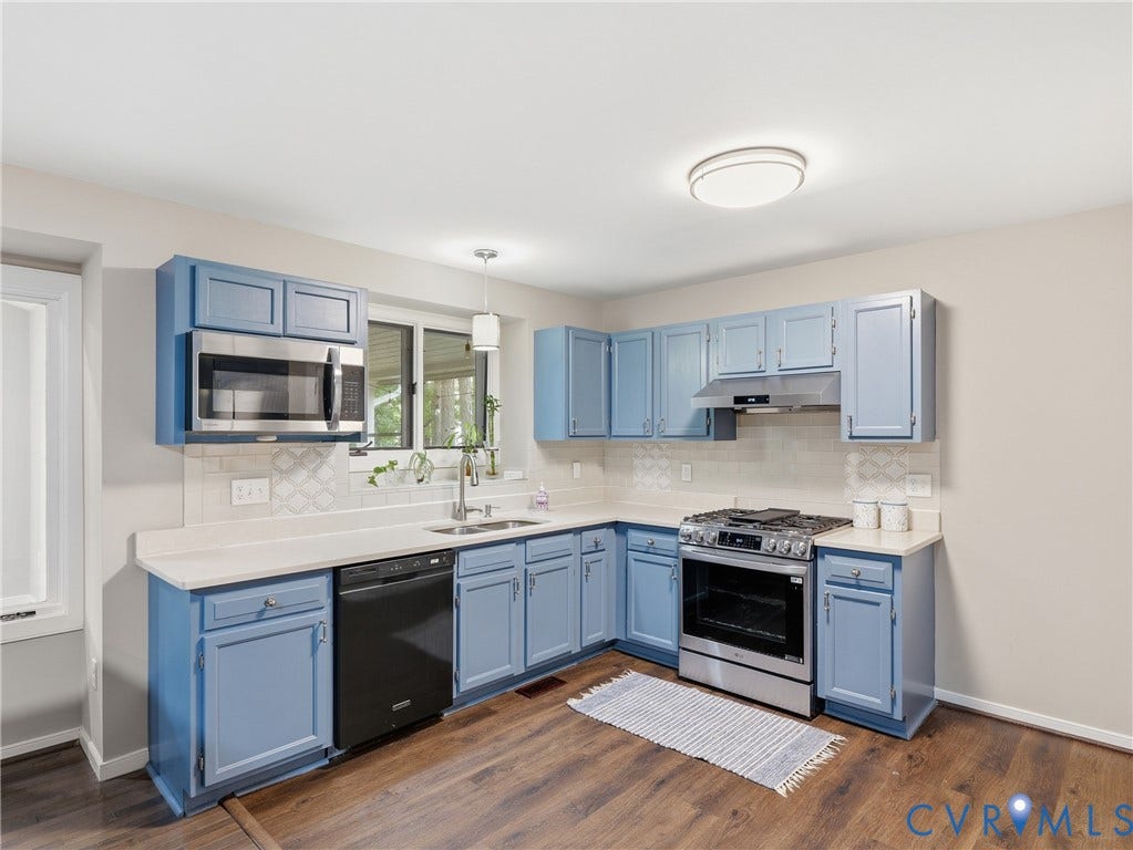 Kitchen featuring blue cabinetry, stainless steel appliances, a white countertop, patterned tile backsplash, and wood-finish flooring
