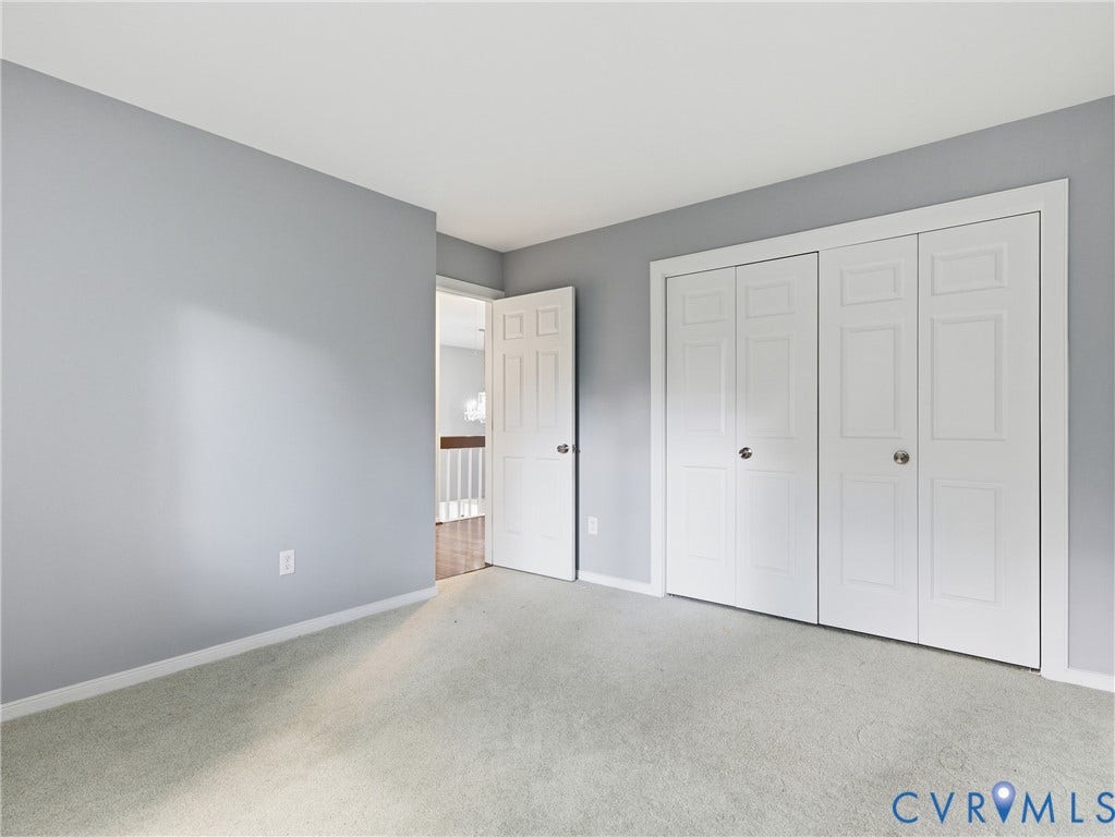 Light gray wall paint, white trim, light-colored carpet flooring, white bi-fold closet doors, and a white interior door