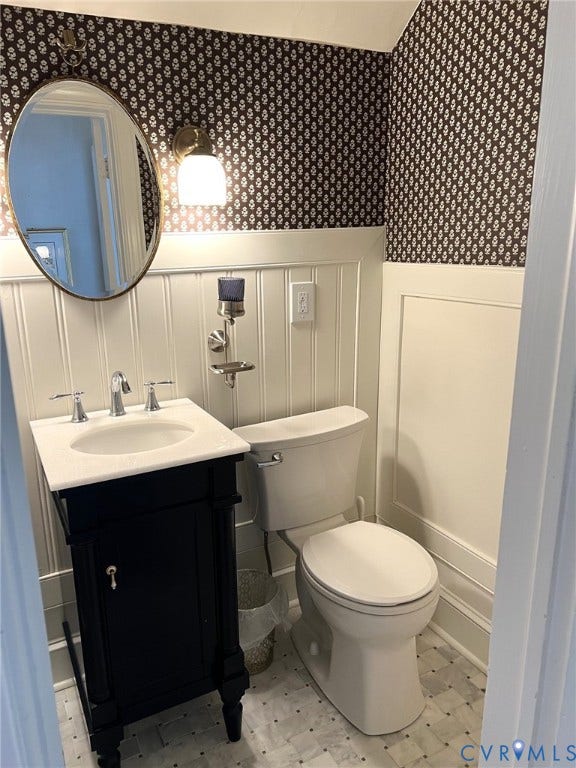 7134 Messer Road, Henrico, VA 23231 Black vanity with a white countertop and undermount sink, patterned wallpaper, beadboard wainscoting, and mosaic tile flooring