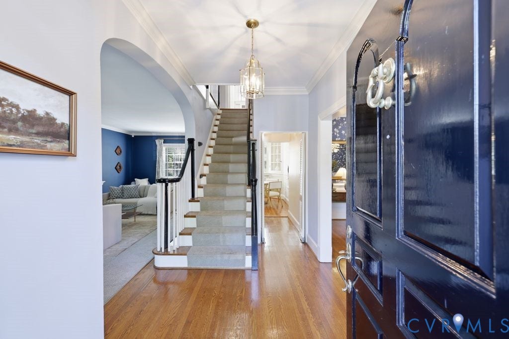 4117 W Franklin Street, Malvern Gardens, Richmond, VA 23221 Hardwood flooring, arched doorway, panel-style front door, built-in staircase with white risers and dark wood handrail, and an overhead chandelier
