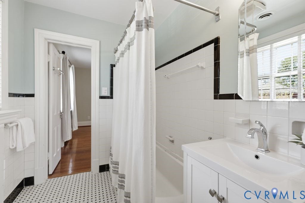 4117 W Franklin Street, Malvern Gardens, Richmond, VA 23221 Bathroom featuring a white tile tub surround with black accent tile, a white vanity with an integrated sink, a chrome faucet, and a black and white mosaic tile floor