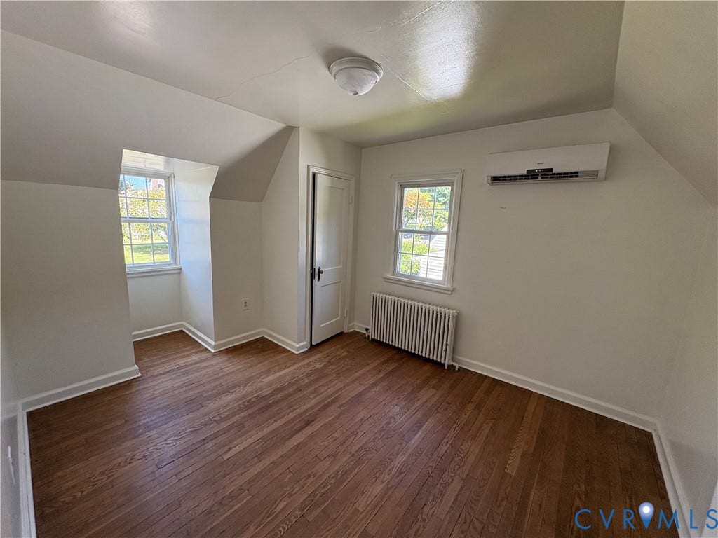 6211 Clover Lane, Lakeside, Henrico, VA 23228 Bright upper-level bedroom featuring wood-finish flooring, multiple windows with natural light, a wall-mounted split-system air conditioning unit, and a radiator heating system