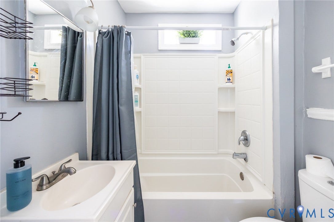 3505 Meadowbridge Road, Richmond, VA 23222 Bright, updated bathroom featuring a white ceramic pedestal sink with chrome faucet, a combined tub and shower enclosure with white tile surround, recessed shelving for storage, and a gray tile accent wall