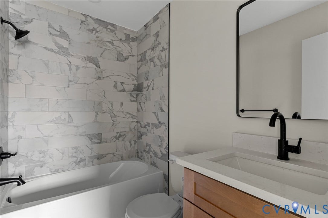 3924 Lamplighter Drive, Richmond, VA 23234 Bathroom featuring a combined tub and shower with marble-look subway tile surround, matte black fixtures, a floating wood-finish vanity with an integrated sink, and a framed mirror
