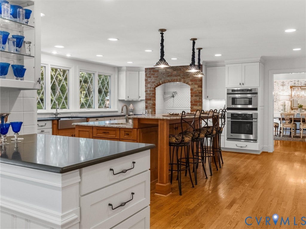 500 Kilmarnock Drive, Collegiate Area, Henrico, VA 23229 Wood-finish flooring, white cabinetry, a brick archway with a tiled backsplash, built-in stainless steel appliances, and an island with a breakfast bar