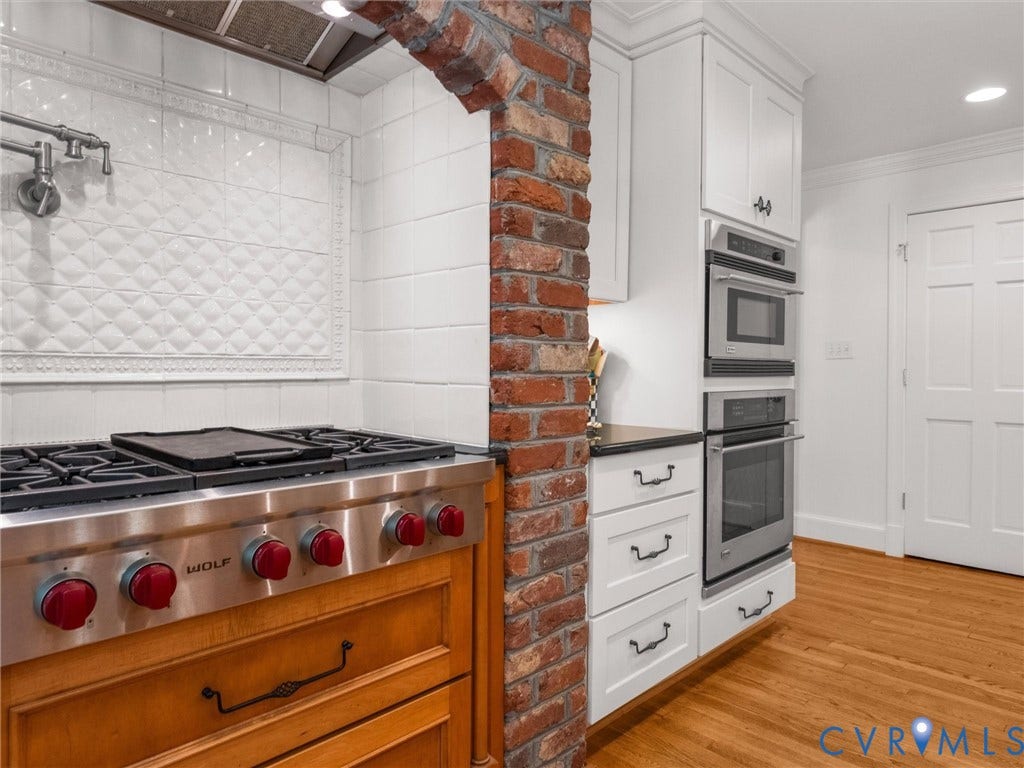 500 Kilmarnock Drive, Collegiate Area, Henrico, VA 23229 Stainless steel range with red knob accents, brick archway, white cabinetry, integrated stainless steel microwave and oven, and wood-finish flooring