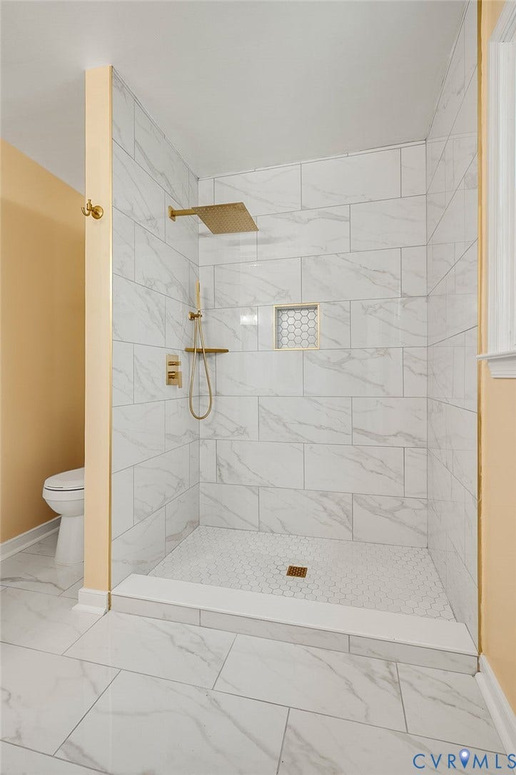 Walk-in shower with large format wall tiling, hexagonal floor tiling, recessed shower niche, and a gold-toned rain showerhead