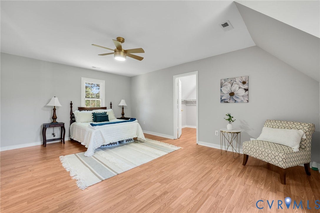 Spacious primary bedroom with vaulted ceilings and ceiling fan, hardwood flooring throughout, and abundant natural light from multiple windows