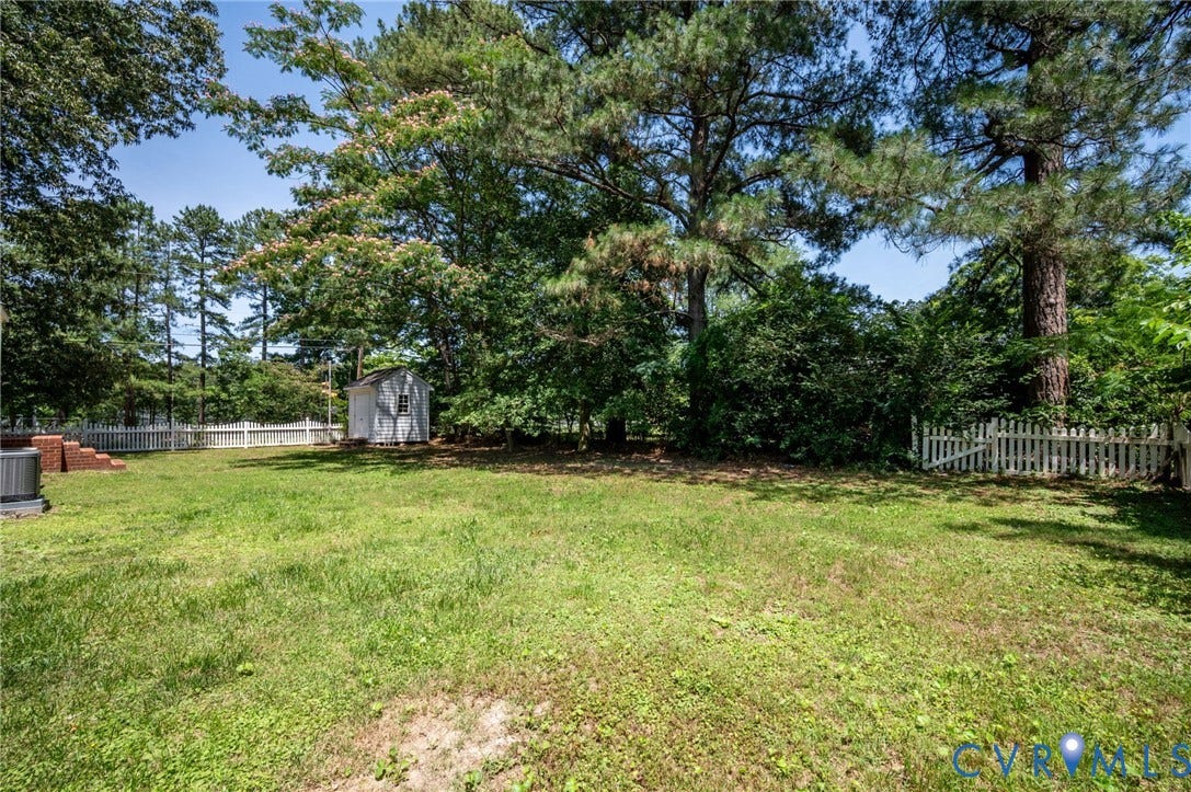Expansive green lawn with mature trees, a white picket fence, and a storage shed