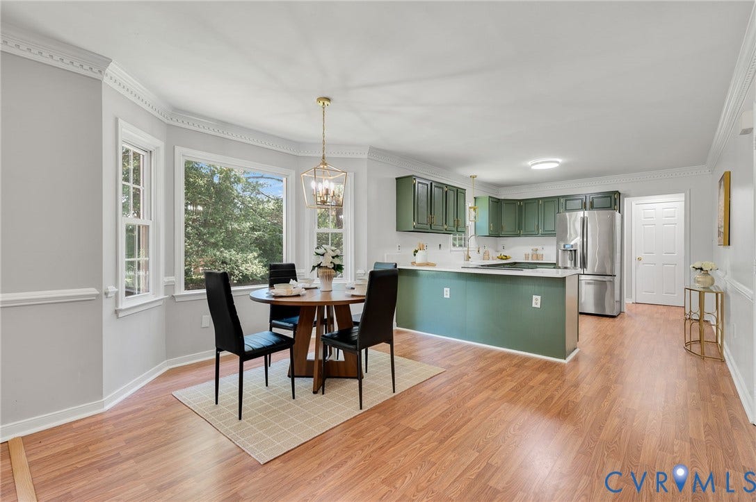 Bay window with decorative crown molding, wood-finish flooring, kitchen with green cabinetry, white countertops, and stainless steel appliances
