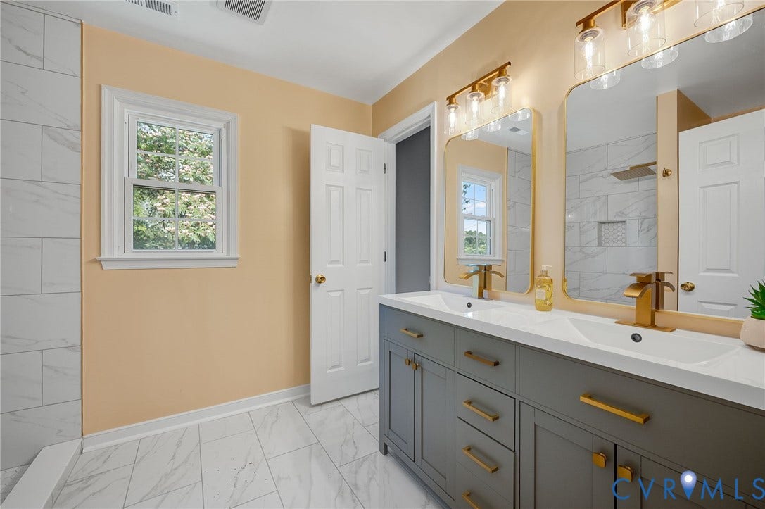 Double vanity with undermount sinks, gold-finish fixtures, and a grey cabinet base