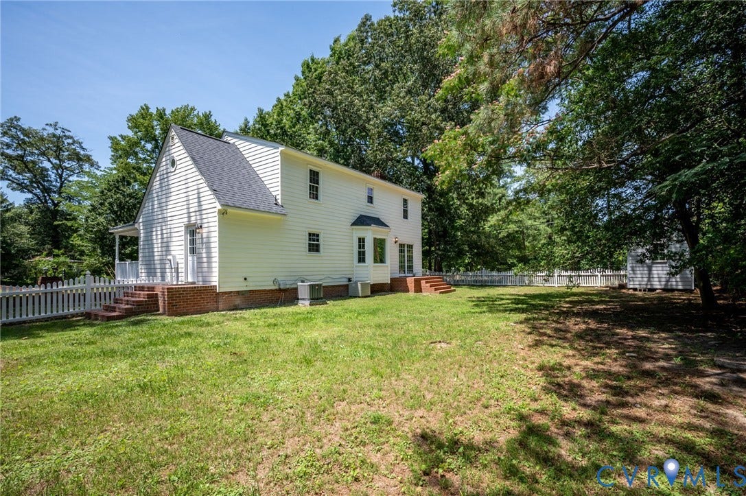 White picket fence enclosing a spacious grassy yard, featuring a siding exterior, gabled roof, and a bay window