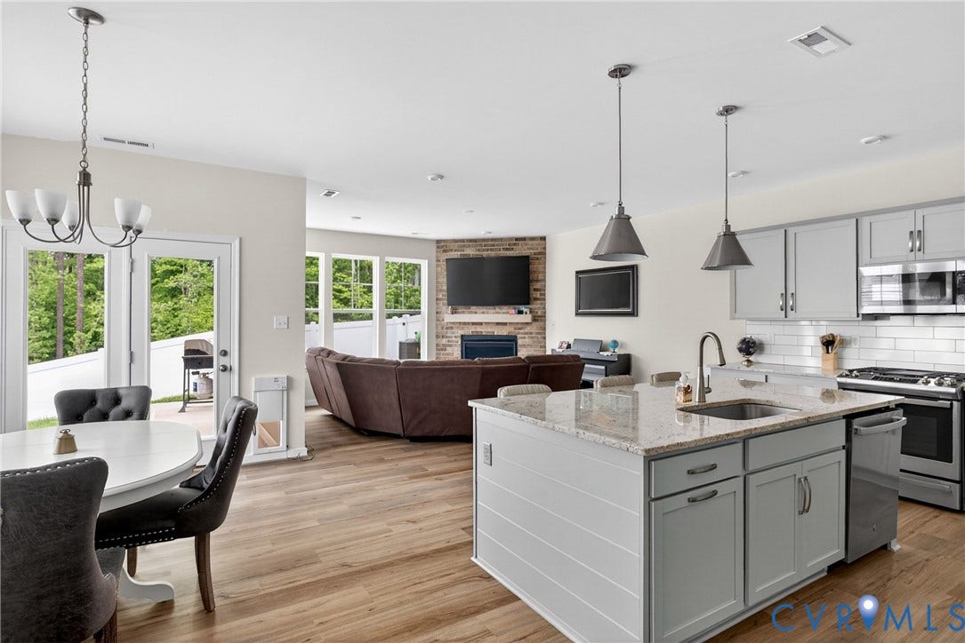 3700 Irby Pond Drive, Midlothian, VA 23112 Open-concept living space featuring wood-finish flooring, a kitchen island with stone countertop, stainless steel appliances, and a brick-accented fireplace