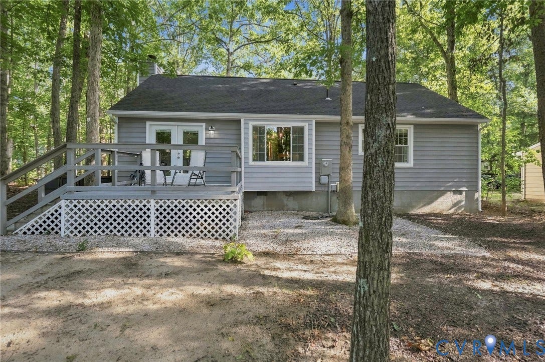 13700 Carriage Creek Place, Chesterfield, VA 23112 Rear exterior featuring a grey wood-sided structure, a grey shingled roof, a grey deck with white lattice skirting, double glass doors, and a window with white trim