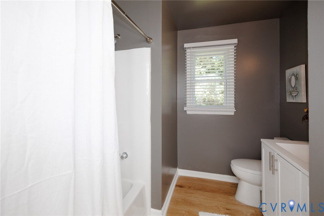 20520 Cox Road, Sutherland, VA 23885 White bathtub with shower, wood-finish flooring, white vanity with integrated sink, toilet, and a window with blinds