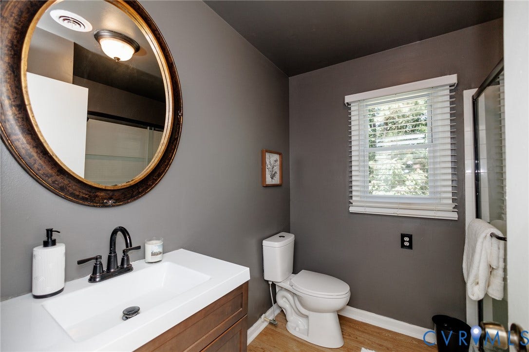 20520 Cox Road, Sutherland, VA 23885 Bathroom featuring a wood-finish vanity with a white countertop, an oval mirror, a window with blinds, and wood-finish flooring