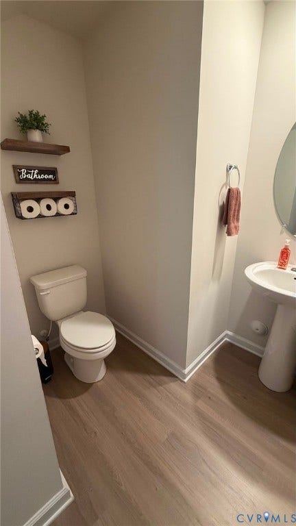 Pedestal sink with an oval mirror, wood-finish flooring, and white baseboards