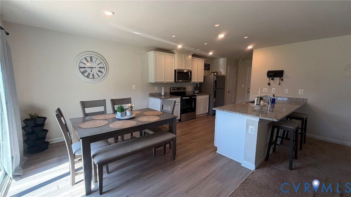 Recessed lighting illuminates the open-concept dining area and kitchen, featuring wood-finish flooring, white cabinetry, and stainless steel appliances