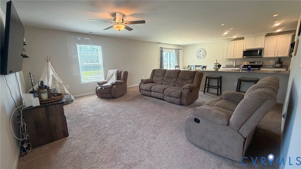 Open-concept living area with carpet flooring, a ceiling fan, and a window with blinds