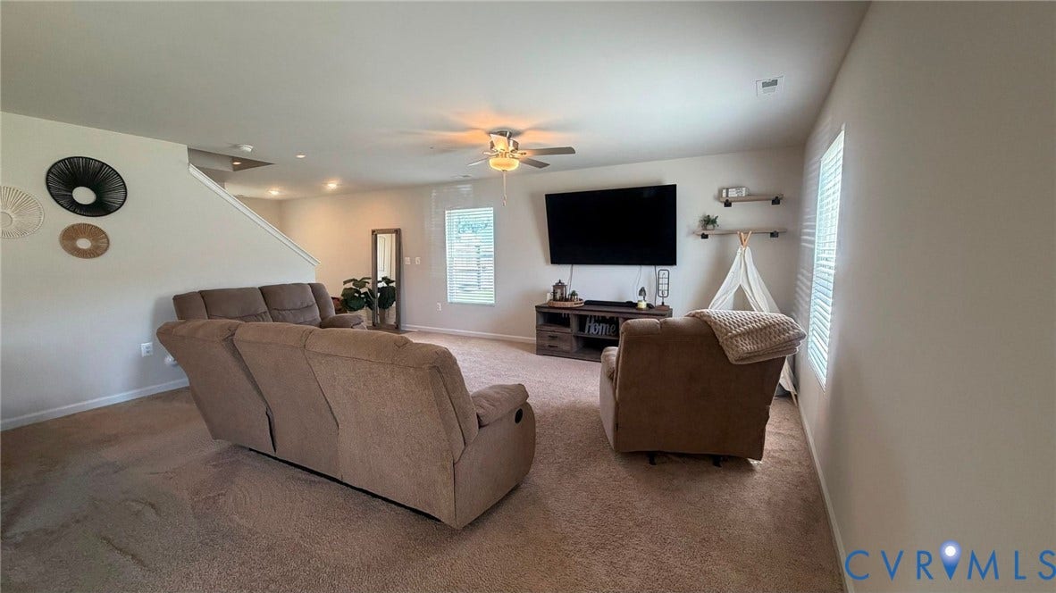 Spacious living area with carpeted flooring, a ceiling fan with integrated lighting, recessed lighting, and a prominent window providing natural illumination