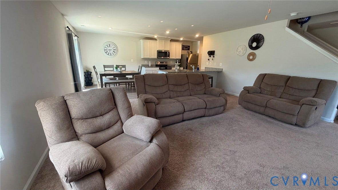 Open-concept living space with recessed lighting, carpeted flooring, and a kitchen featuring light cabinetry, stainless steel appliances, and a breakfast bar