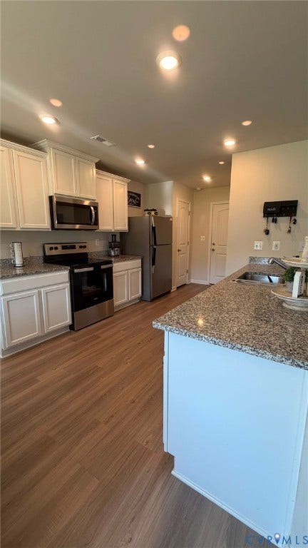 Kitchen featuring wood-finish flooring, white cabinetry, granite countertops, and stainless steel appliances