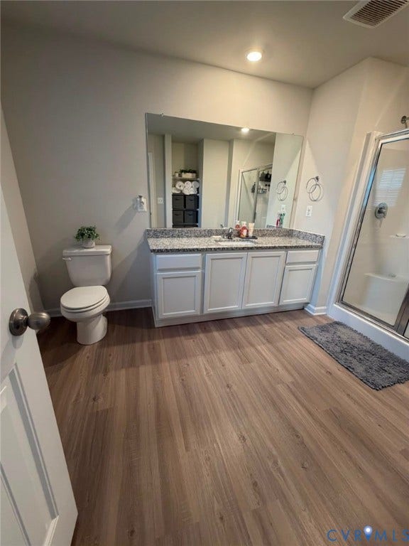 Wood-finish vinyl flooring, white vanity with ample storage, granite-style countertop, large wall mirror, and glass-enclosed shower