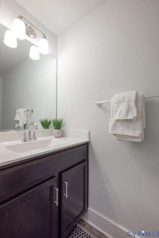 Vanity with dark wood cabinetry and brushed nickel hardware, integrated sink, and white countertop