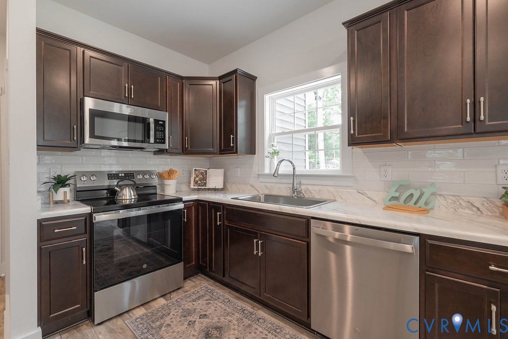 Kitchen featuring dark wood cabinetry, white countertops, stainless steel appliances, white subway tile backsplash, and a stainless steel sink
