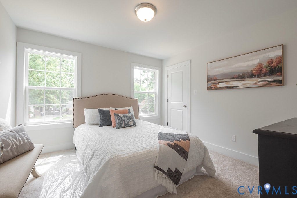 Neutral wall color, two large windows, white trim throughout, carpeted flooring, and a flush mount ceiling light
