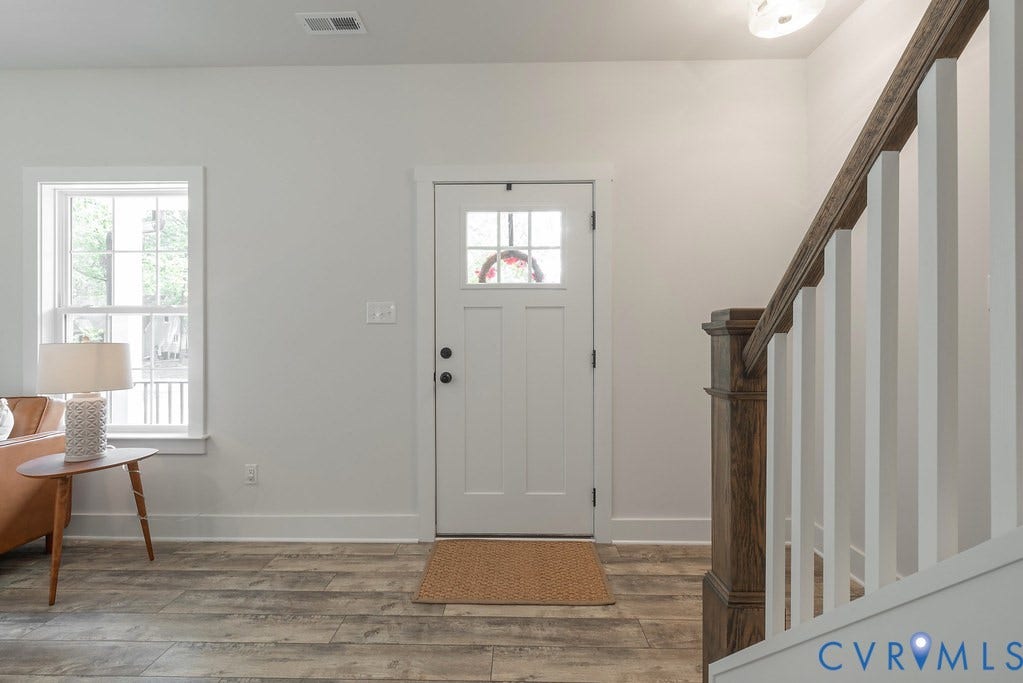Craftsman-style entry door with glass panels, wood-finish flooring, white walls, and a staircase with a wood newel post and handrail