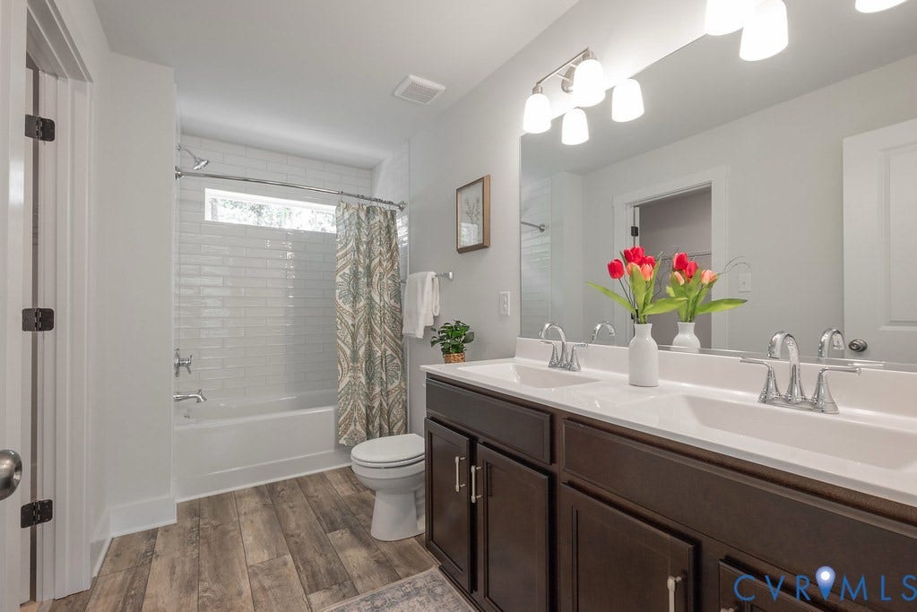 Double vanity with dual sinks, wood-finish flooring, white subway tile shower surround, and a tub-shower combination