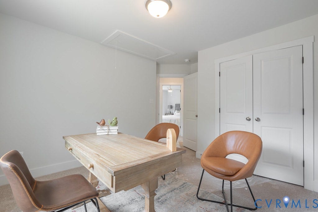 Bright, light-filled office space featuring a light wood desk with storage drawers, warm cognac-leather accent chairs, and white panel closet doors