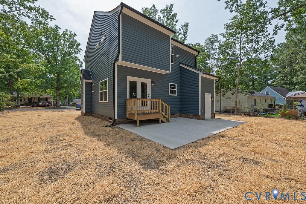 Siding exterior, concrete patio, double exterior doors, wooden deck with railing, and perimeter trees