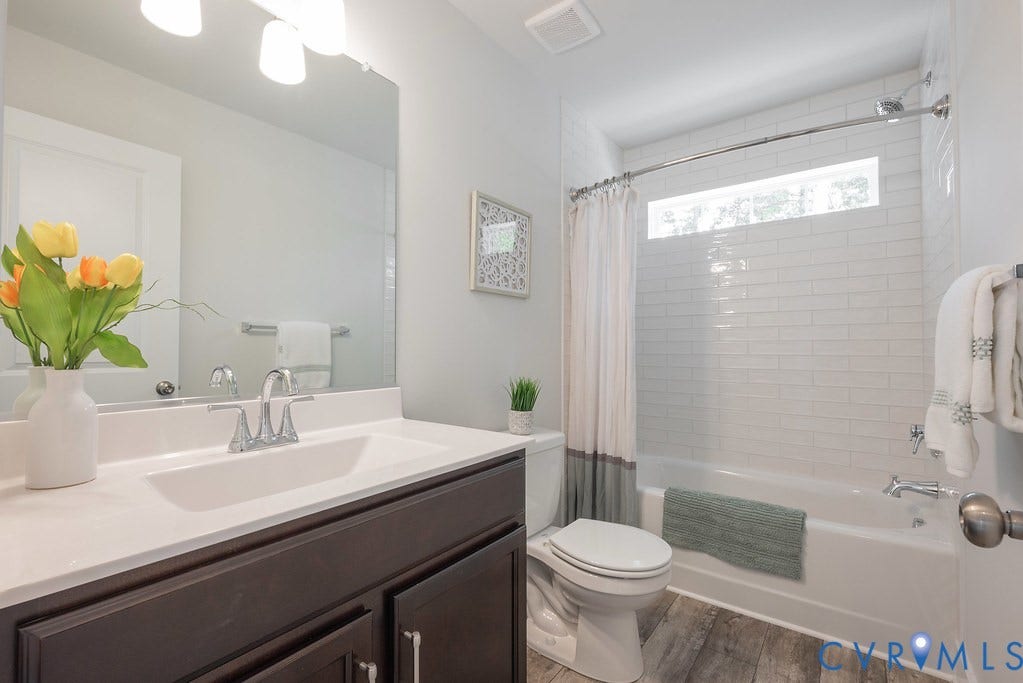 Bathroom featuring a wood-finish floor, dark wood-finish vanity with an integrated white sink, chrome fixtures, and a subway tile tub surround
