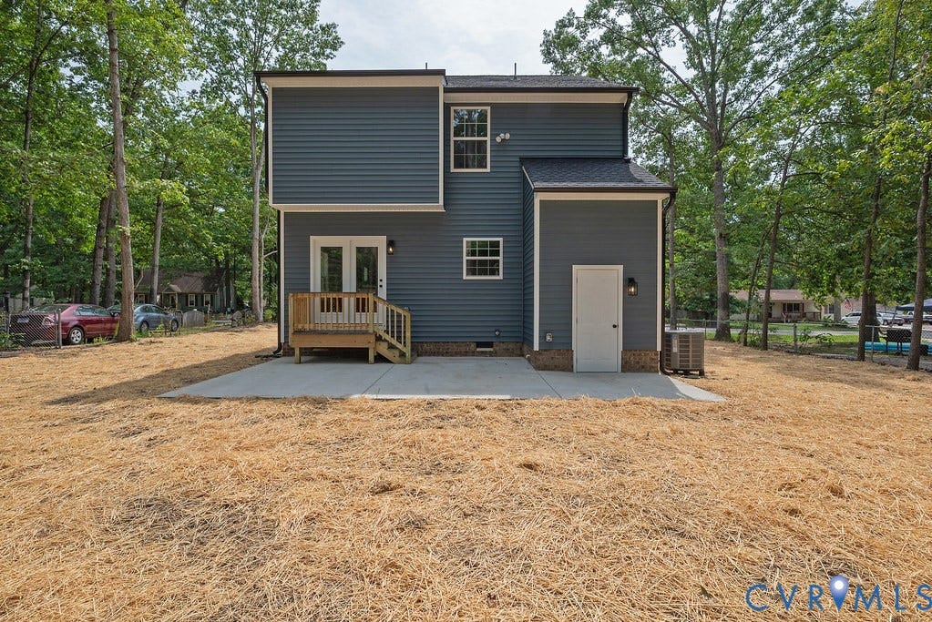 Two-story residence with blue siding, wood deck with stairs, concrete patio, and a side entry door