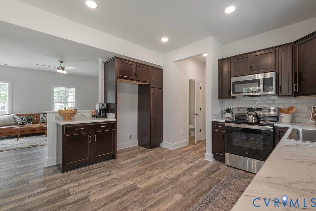 Kitchen featuring wood-finish flooring, dark wood cabinetry, light-toned countertops, subway tile backsplash, and stainless steel appliances