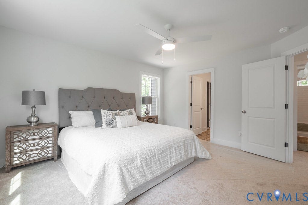 Neutral tone wall paint with white trim, light-colored carpeting, two white paneled doors, and a ceiling fan with integrated lighting