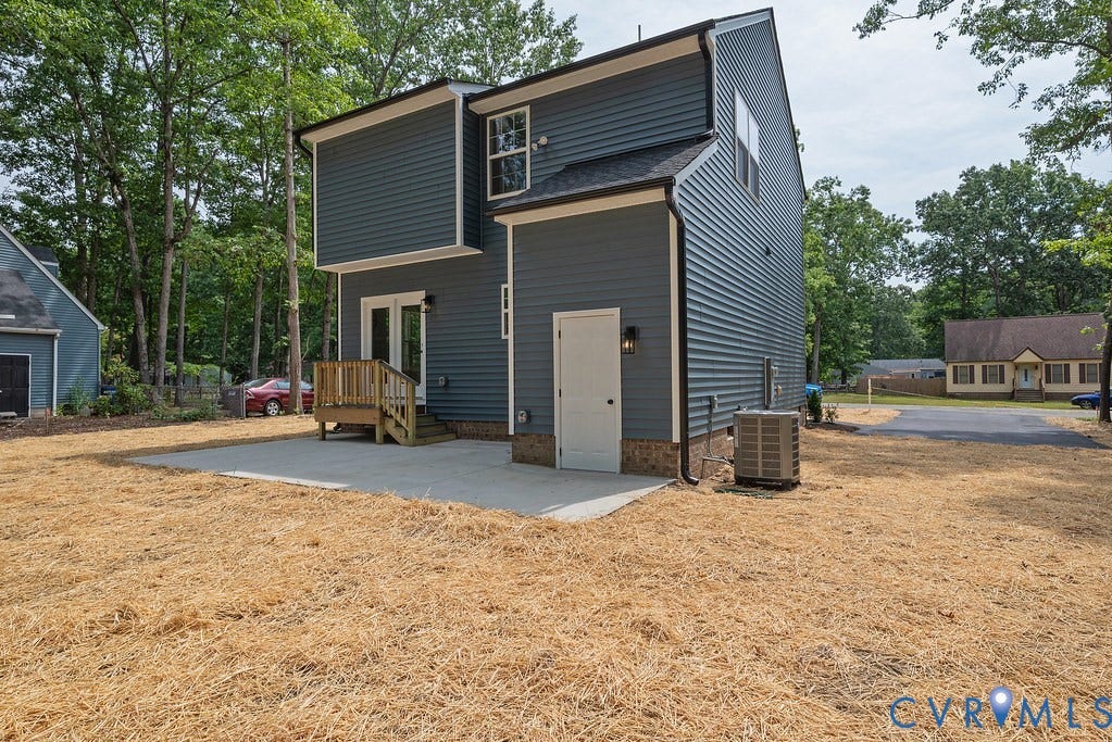 Contemporary dark gray siding exterior with white trim, featuring a private rear patio, wooden deck with railing, and an exterior storage door